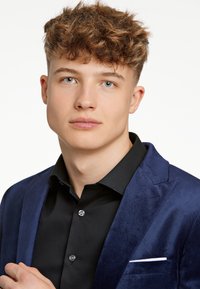 Mörkblå sammet blazer med en svart skjorta. Blazern har en vit fickhandduk och har en notch lapel-design.