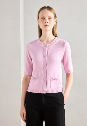 Cardigan rose à manches courtes avec encolure côtelée et boutonnière. Présente deux poches avant ornées de boutons décoratifs. Texture douce.