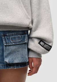 Felpa grigia con tasca a marsupio e polsini a coste, abbinata a una gonna di jeans con tasca applicata e cuciture a contrasto.