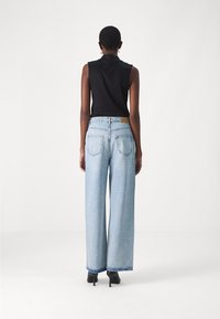 Jeans a vita alta di colore azzurro chiaro con gamba larga e orlo sfilacciato. Indossati con un top senza maniche nero, che mette in evidenza una silhouette liscia e aderente.
