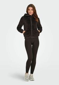Sort, fluffy hættejakke med lynlås, to frontlommer, ribbede manchetter, parret med sorte leggings og lysegrå løbesko.