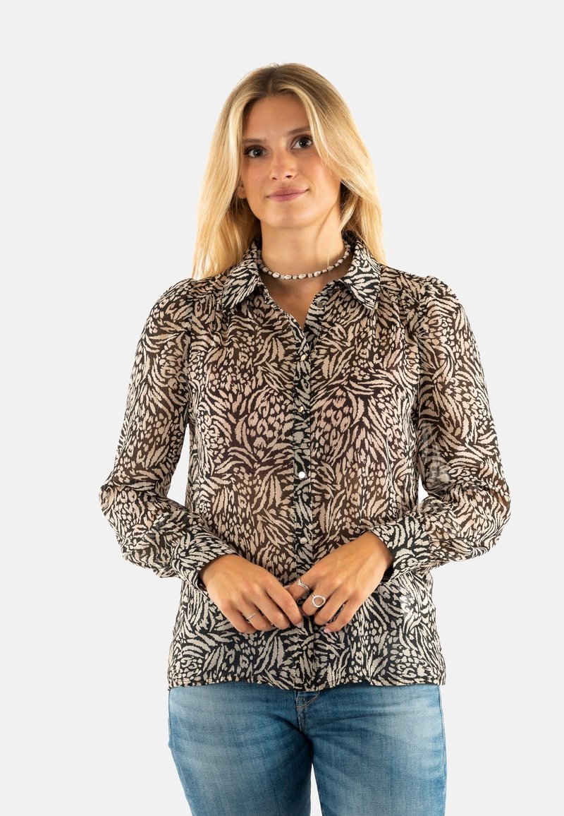Blusa trasparente nera e beige con un motivo astratto a foglia, chiusura con bottoni frontale, maniche lunghe e colletto classico. Abbinata a jeans blu.