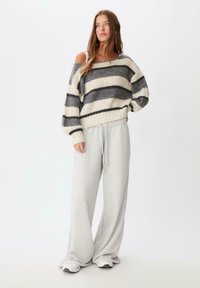 Oversized sweter w paski w kolorze szarym i kremowym, ribbowana tekstura i designerski krój z odsłoniętymi ramionami, w połączeniu z szerokimi spodniami dresowymi w kolorze szarym.