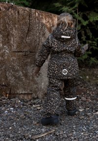 Gepolsterter Schneeanzug mit Leopardenmuster in Braun und Schwarz, ausgestattet mit Kapuze, elastischem Bund und reflektierenden Akzenten. Schwarze wasserdichte Stiefel.