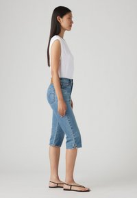 Bijela bezrukavna majica, plave traperice srednjeg struka s isfrkanim rubovima i bočnim prorezima, uparene s crnim sandalama. Jednostavan, ležeran outfit.