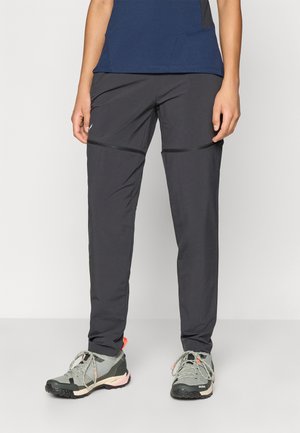 Μαύροι ελαφριοί παντελόνες με στενή εφαρμογή, με οριζόντια ραφή και μικρό λογότυπο στο αριστερό μηρό, σε συνδυασμό με γκρι παπούτσια πεζοπορίας.