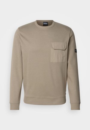 Beige puuvillane dressipluus pikkade varrukatega, ümmarguse kaelaauguga, soonikuga mansettide ja alumise servaga, ning vasakul rinnal on esikott.