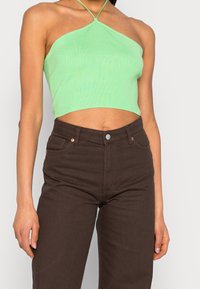 Zielony prążkowany krótki top z dekoltem halter, zestawiony z ciemnobrązowymi, wysokowzrostowymi jeansami z przednimi kieszeniami i metalowym zapięciem na guziki.