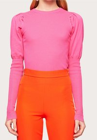 Pull côtelé ajusté de couleur rose vif avec épaules bouffantes et manches longues, associé à un pantalon orange taille haute.