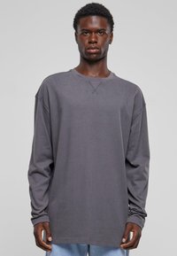 Grå genser med lange ermer i myk bomull, med rund hals og senket skuldre, som har subtile sømmer. Brukt med blå jeans.