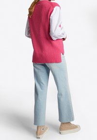 Rosa gerippter Pullover, über einem weißen Shirt getragen, kombiniert mit hellblauen geraden Jeans und beigen High-Top Sneakern.