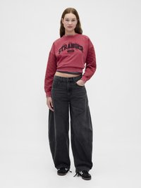 Sudadera roja recortada con mangas acolchadas que presentan el texto "STRANGER THINGS", combinada con jeans de mezclilla negros holgados y zapatillas negras.