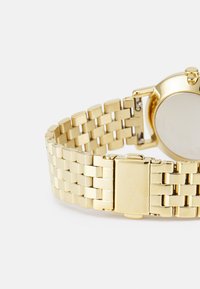 Hodin g z nerezové oceli se zlatým tónem a pleteným náramkem, s kulatým pouzdrem a leštěným povrchem. Spona s vyrytým názvem značky.