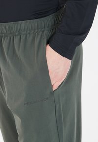 Gröna joggingsbyxor med elastisk midja, sidoficka och "ENDURANCE"-logotyp nederst till vänster. Mjuk, lättviktsmaterial.