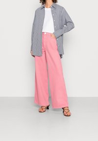 Striped blue and white oversized shirt, white t-shirt underneath, and wide-leg pink jeans; textured fabric, casual fit, and open collar.