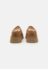 Chaussures décontractées en daim brun avec une doublure intérieure douce, semelle plateforme et logo UGG à l'arrière. Texture lisse et forme arrondie.