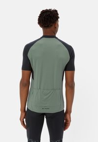 Zielona koszulka rowerowa z krótkim rękawem, z czarnymi rękawami raglanowymi, teksturowana tkanina i tylna kieszeń na akcesoria. Logo umieszczone na dolnej krawędzi.