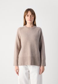 Beige pletený svetr s kulatým výstřihem, dlouhými rukávy a žebrovaným lemem. Má jemnou texturu a vzorované detaily na ramenou.