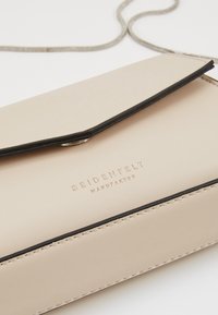 Borsa a tracolla in pelle beige con dettagli neri, dotata di chiusura a patta e logo in rilievo. Texture liscia e linee pulite.