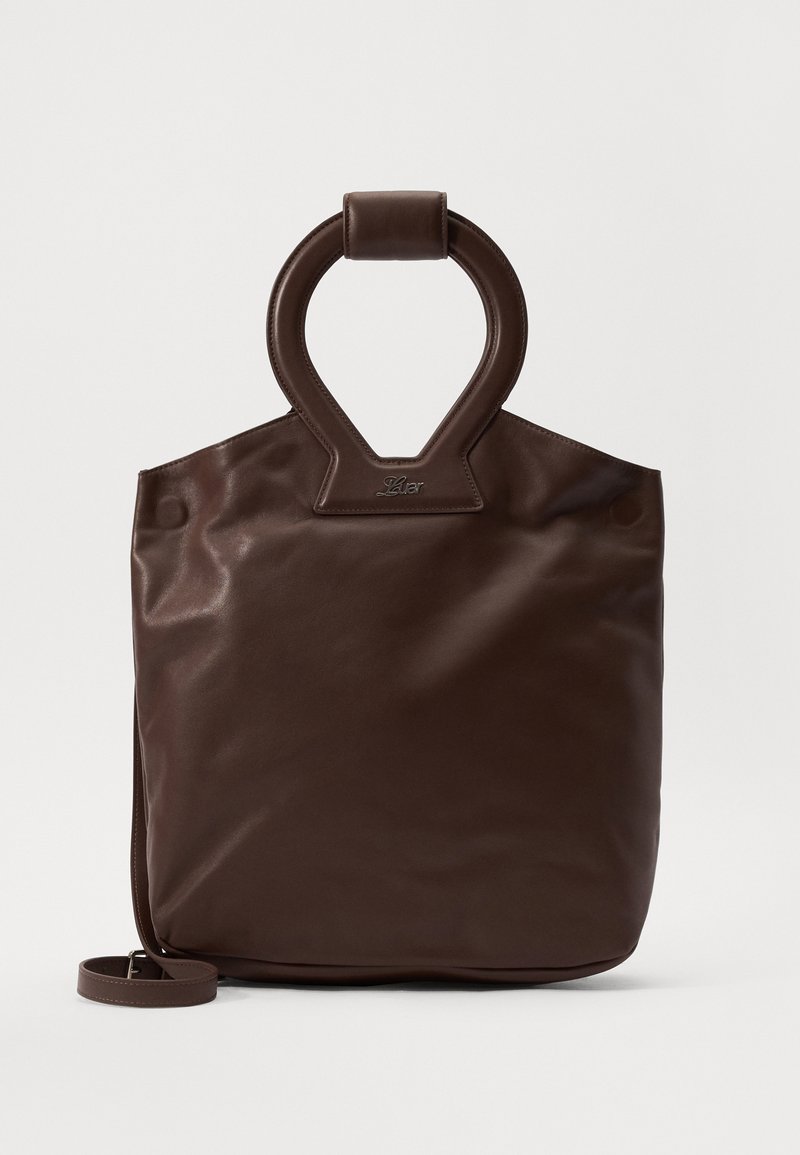 Sac tote en cuir marron avec une poignée supérieure ovale, texture lisse, fermeture éclair et une bandoulière amovible. Design minimaliste.