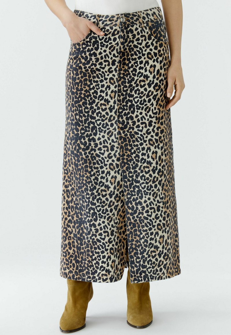 Maxikleid mit Leopardenmuster in Beige, Braun und Schwarz, ausgestattet mit Seitentaschen und einem geraden Schnitt. Kombiniert mit olivfarbenen Stiefeletten.