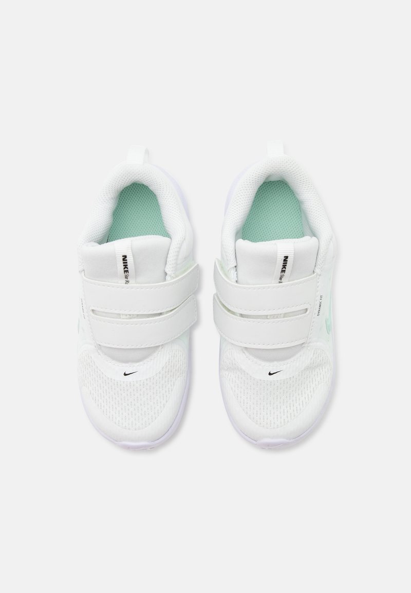 Λευκά παιδικά παπούτσια Nike με σόλες εσωτερικά σε χρώμα μέντας, πλέγμα στα δάχτυλα και διπλά ρυθμιζόμενα λουριά βέλκρο, απεικονισμένα από πάνω.