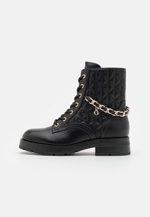 Black ankle boots with a quilted texture, gold eyelets, and a chain accent. Slightly rounded toe, flat rubber sole, and mid-height shaft.