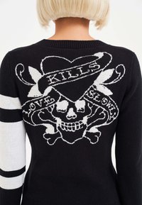 Black knitted sweater featuring a white skull and crossbones design with "KILLS" and "LOVE" text. White stripes on sleeves add contrast.