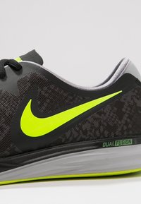 Černá sportovní bota s Texturovanou látkou, jasně žlutý „Swoosh“ Nike, šedé detaily a šedá podrážka s nápisem "DUAL FUSION."