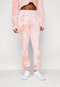 Rosa tie-dye joggebukser med elastisk midje og mansjetter. Mykt stoff, med en blanding av lyse og mørkere rosa nyanser. Kombinert med hvite sneakers.