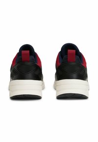 Un paio di sneakers nere, rosse e blu con suole bianche spesse, viste da dietro su uno sfondo bianco.