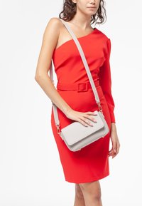 Borsa a tracolla grigia con una finitura testurizzata e chiusura a coperchio, abbinata a un vestito rosso aderente con scollatura asimmetrica.