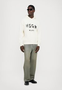 Felpa con girocollo di colore avorio con grafica nera "MSGM MILANO". Abbinata a jeans dritti verde sbiadito e scarpe nere.