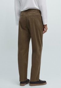 Bruine, comfortabele broek met elastische tailleband, voorzien van twee achterzakken en een soepele textuur, gecombineerd met donkere schoenen.