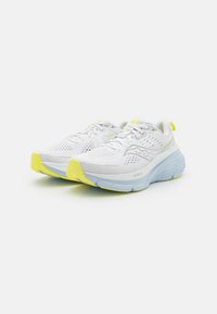 Hvite joggesko med mesh-overdel, teksturerte detaljer og gule aksenter på sålen. Lett design med polstret mellomsåle.