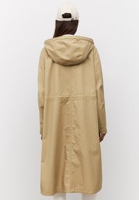 Abrigo largo beige con capucha, que presenta una cintura ceñida, mangas rectas y tejido texturizado. La vista trasera muestra un diseño simple y minimalista.