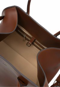 Interieur van een bruine leren tote bag met een beige voering, een ritscompartiment en een centrale scheiding met een sleutelhangerbevestiging.