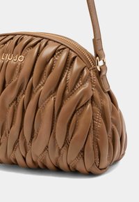 Sac à main en cuir matelassé marron avec une forme arrondie, un motif torsadé décoratif et des accents en métal doré. Fermeture à glissière avec une bandoulière.