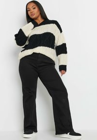 Stickad tröja i svart och gräddfärgad rand med kabelstickat mönster, kombinerad med svarta raka byxor och svarta sneakers.