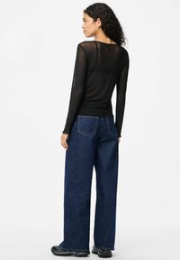 Svart långärmad topp med en genomskinlig, prickig textur, i kombination med mörkblå vida jeans och svarta skor. Enkel design, inga synliga logotyper.