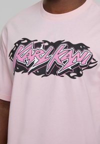 Pink cotton t-shirt featuring a bold black and pink graphic logo with flame accents. Round neckline and short sleeves.