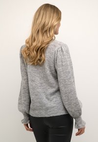 Szary sweter z dzianiny z długimi, bufiastymi rękawami i dopasowanym pasem. Miękka tekstura z delikatnym wzorem. Stylizowany z czarnymi spodniami.