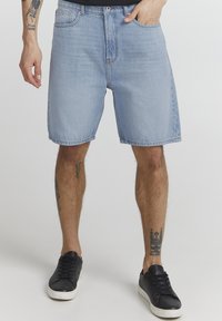 Shorts en denim bleu clair à coupe décontractée, avec poches avant et fermeture à un bouton. Associés à des baskets noires basses.