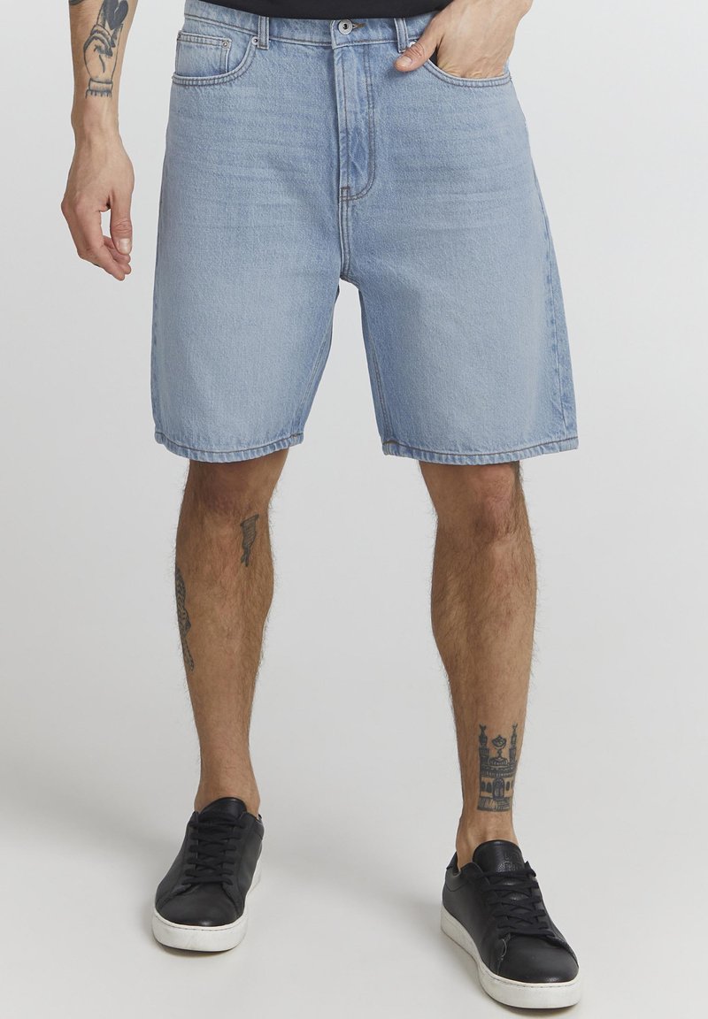 Shorts di jeans azzurri chiari con vestibilità rilassata, tasche frontali e chiusura con un solo bottone. Abbinati a sneakers nere basse.