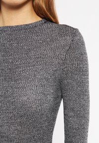 Grå ribbade stickade tröja med hög krage, med en texturerad design och långa ärmar. Tyget verkar mjukt och lätt.