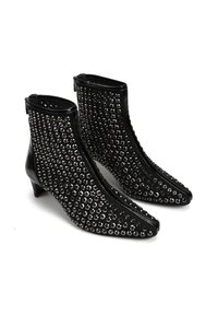 Czarne botki na kostkę wykonane z błyszczącego materiału, z ostrymi noskami pokrytymi metalowymi ćwiekami, z niewielkim obcasem i zamkiem błyskawicznym.
