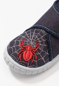Navy canvas shoe featuring a red spider embroidered on a web design. Includes a grey rubber sole and adjustable strap for secure fit.
