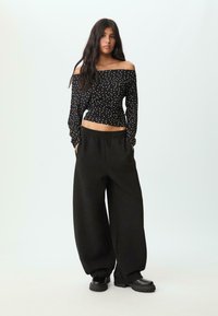 Schwarzes, schulterfreies Oberteil mit weißen Polka-Dots, kombiniert mit lockeren schwarzen Hosen und klobigen schwarzen Schuhen, die einen entspannten Look erzeugen.
