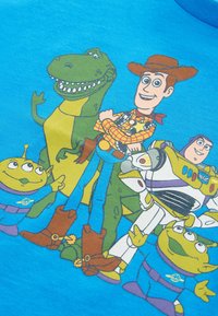Blaues Baumwoll-T-Shirt mit animierten Figuren: einem grünen Dinosaurier, einem Cowboy, einem Astronauten und Aliens, in lebendigen Farben und detaillierten Designs.