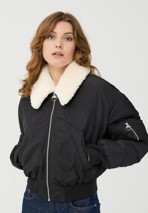 Giacca bomber nera con colletto in finta pelliccia color crema, zip frontale, polsini a costine e tasche laterali. Presenta una piccola tasca con zip sulla manica.